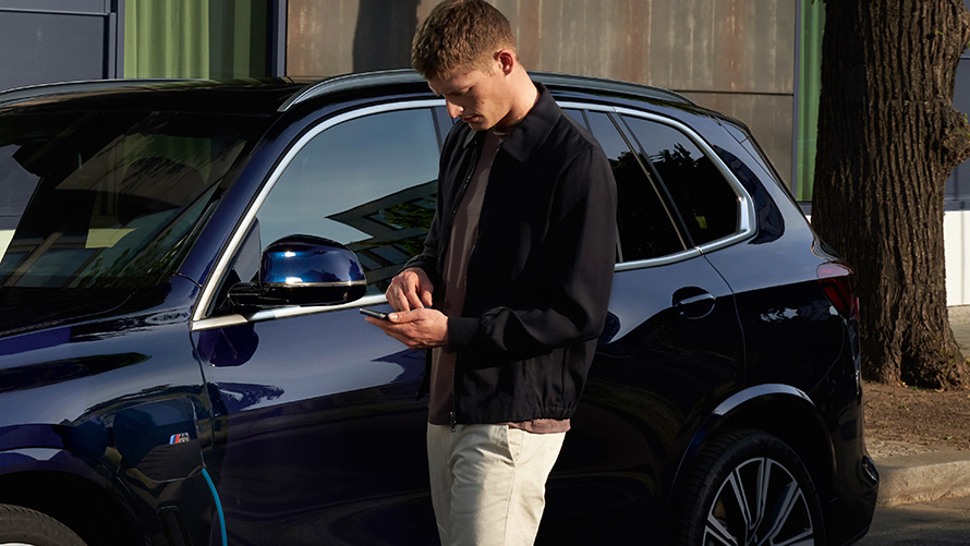 Remote Software Upgrade Muškarac ispred BMW-a gleda u svoj pametan telefon