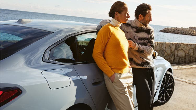 BMW Service Inclusive muškarac i žena naslonjeni na modelu BMW i4 na obali