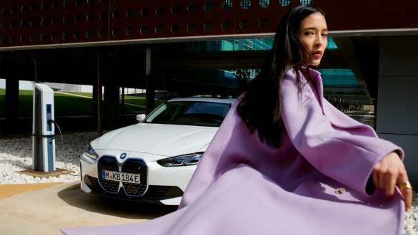 BMW Service Inclusive žena stoji ispred BMW-a i4 na stanici za punjenje